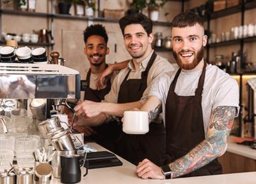 Three male baristas smile and serve coffee