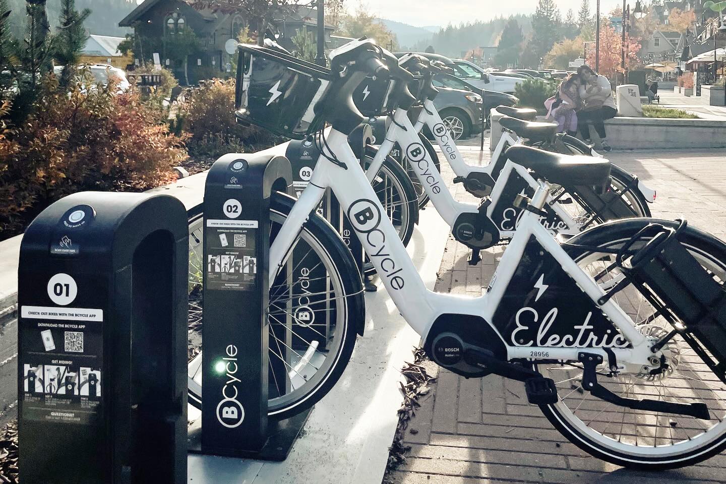 A row of white electric bikes with BCycle written on them docked at charging stations. 