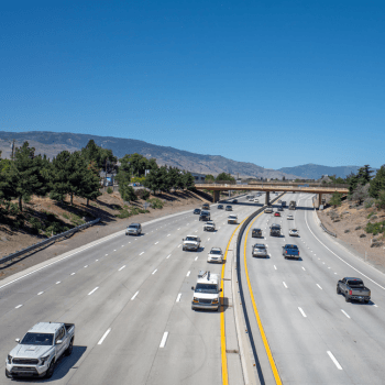 A view of a highway with multiple lanes in both directions with cars and a bridge. 