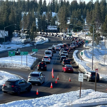 Cars shown bumper to bumper traffic as they go around a roundabout in a snow-covered area. . 