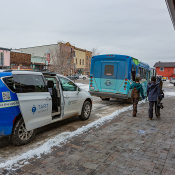 People with snow gear walking from the TART Connect shuttle to the larger fixed route bus. 