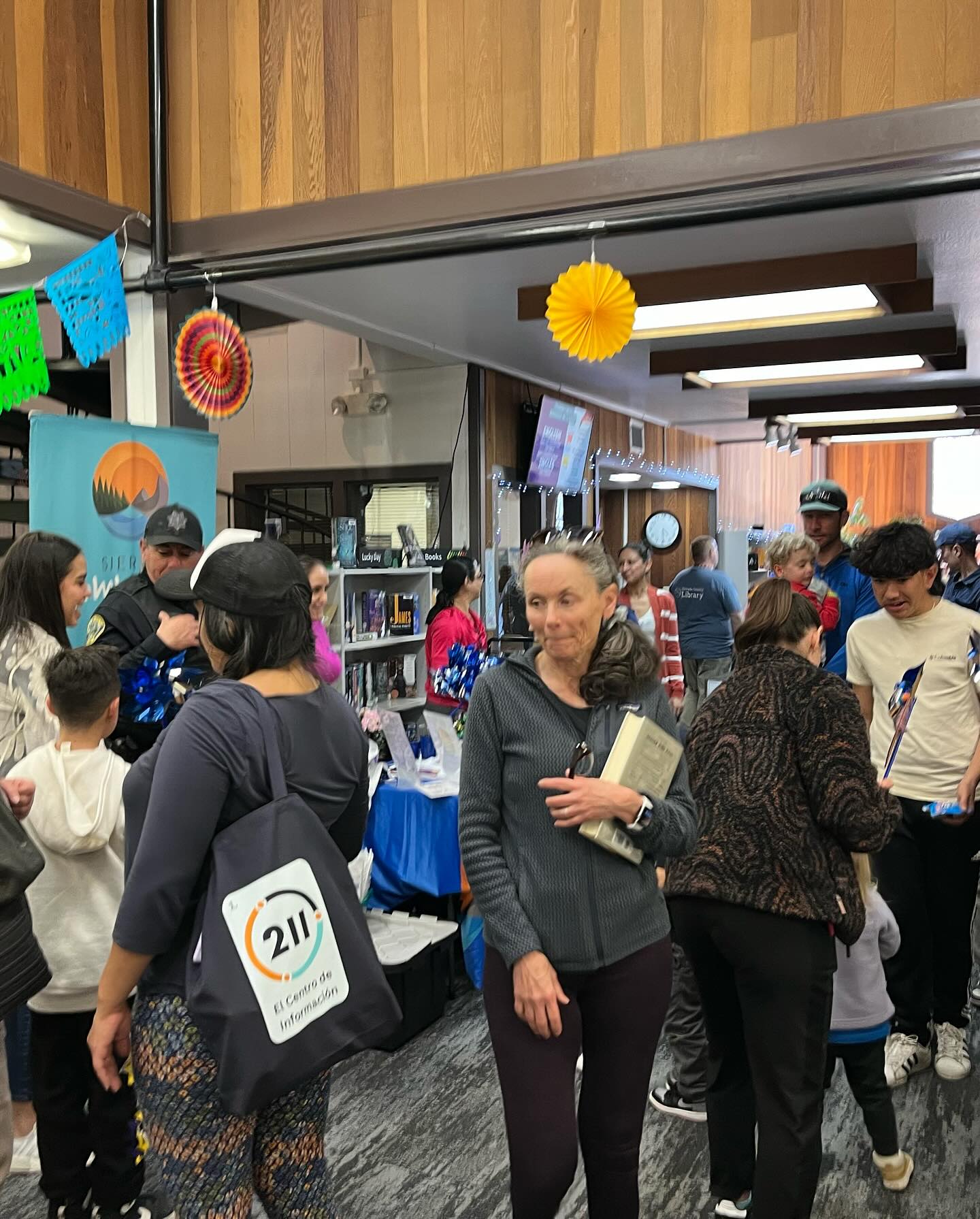 Lots of people walking around an event with stalls in a library. 