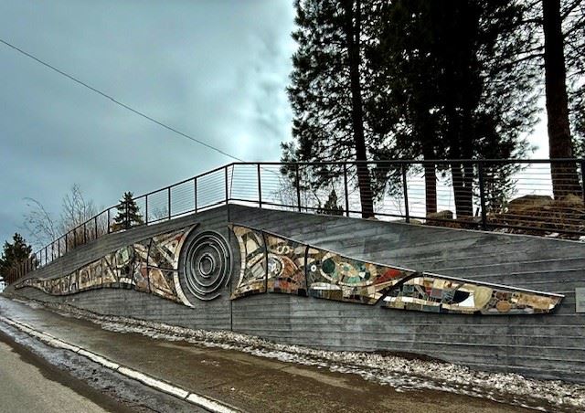 Photo of the PATH sculpture- an abstract shaped sculpture on a wall up a hill by a road.  